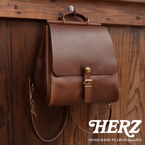 棕色皮革後背包，有頂部提把、可調節肩帶，以及一個帶有金屬扣環的翻蓋式主袋。