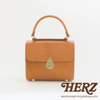 棕色皮革手提包，配有金色鎖扣和提把，底部有四個金色腳釘，展現職人手作質感。