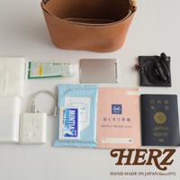 棕色皮革圓筒形收納包，內含濕紙巾、薄荷糖、手機充電器、耳機、化妝品小樣、銀色名片夾和日本護照。