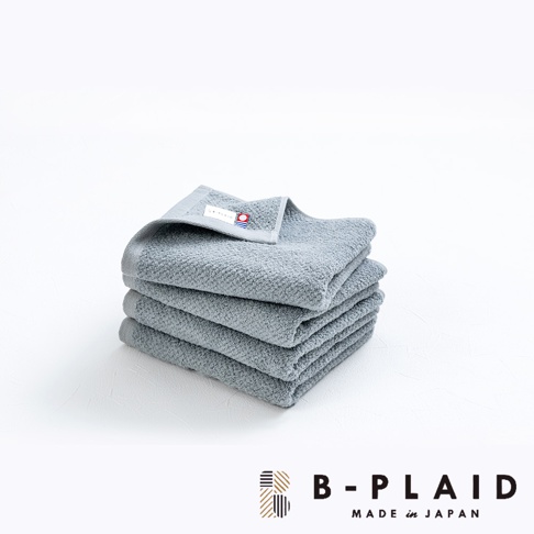 一疊淺灰色的今治毛巾，表面有細緻的鱗紋織紋，其中一條毛巾上縫有品牌標籤。