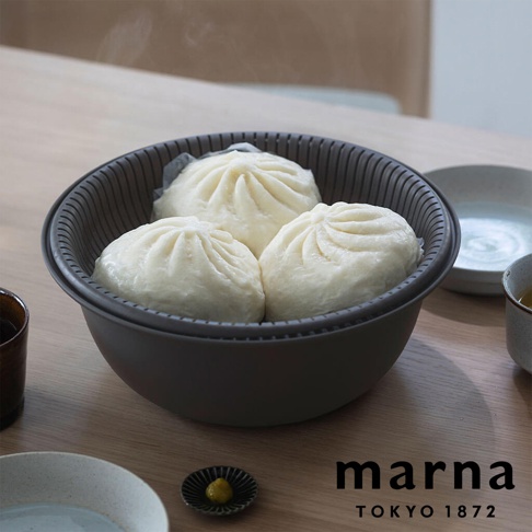 marna TOKYO 1872 品牌標誌旁，是蒸籠裡擺放著三個剛出爐熱氣騰騰的包子，放在深灰色的洗濾盆托盤內，左側有茶杯，右側有水杯。