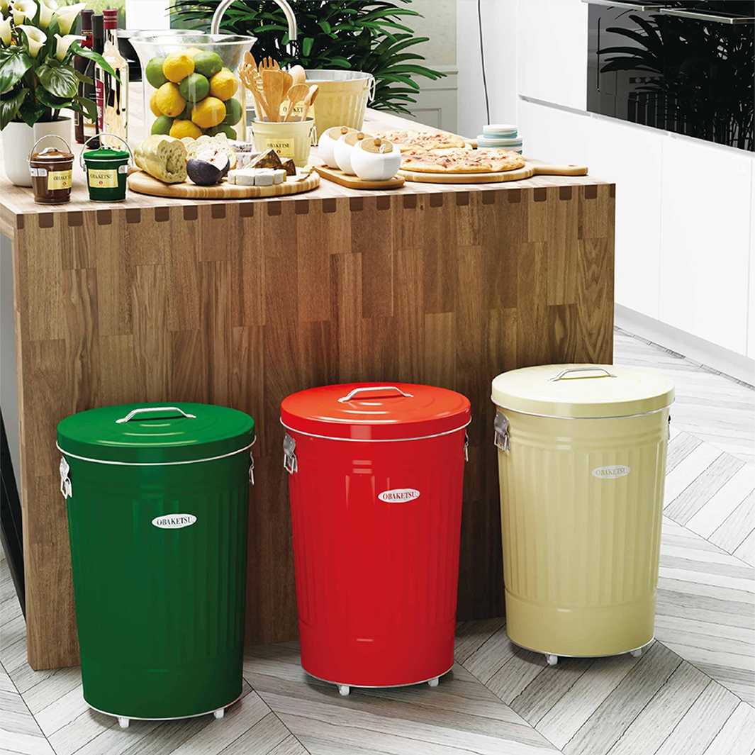綠色、紅色和米黃色的 OBAKETSU 附輪垃圾桶，擺放在木紋餐桌旁。