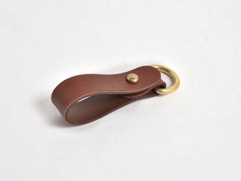 棕色皮革製成的吊掛扣帶，搭配黃銅色金屬環和卯釘，適合鑰匙圈或吊飾。