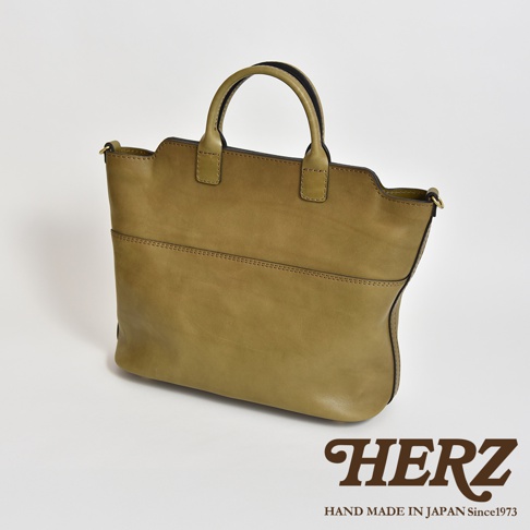 一咖橄欖綠皮革兩用托特包，具有圓潤提把和簡潔線條，包身前方有兩條水平縫線裝飾，材質呈現自然皮革紋理。