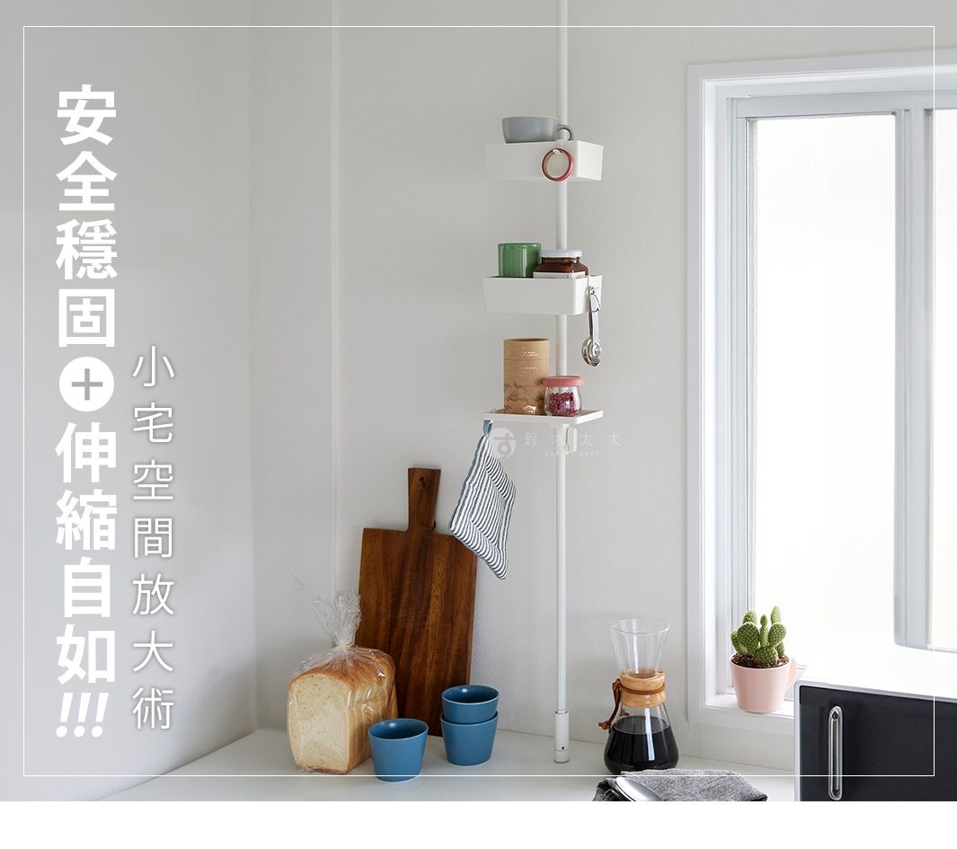 白色伸縮桿直撐於牆壁，頂部裝有白色置物盤，盤上擺放著杯子、綠色罐子、玻璃罐和鑰匙。下方有兩層白色置物盤，分別擺放著罐子、玻璃罐和一條藍白條紋毛巾。桿身旁有木質砧板、一袋麵包和藍色杯子。右側窗台有咖啡濾杯、咖啡壺和仙人掌盆栽。