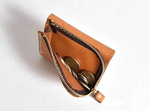 職人手作皮革方形短夾，採用棕色牛皮製作，拉鍊開口設計，內含數枚硬幣，皮革紋理清晰，質樸自然。