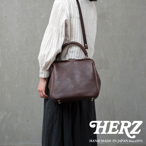 深棕色皮革製成的方形口金托特包，配有可拆卸肩帶和頂部提把，底部有金色金屬腳釘。