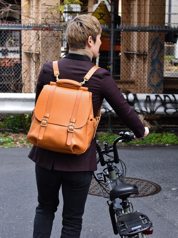 棕色皮革雙扣後背包，帶有頂部提把和可調節肩帶，背包前方有兩個金屬扣環。