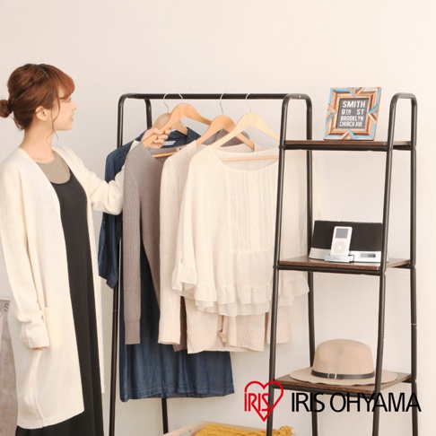 獨特的木板風格分層收納吊掛衣架，金屬黑色支架搭配木紋層板，掛有三件不同顏色的衣物：牛仔洋裝、灰色針織衫及米白色雪紡上衣。