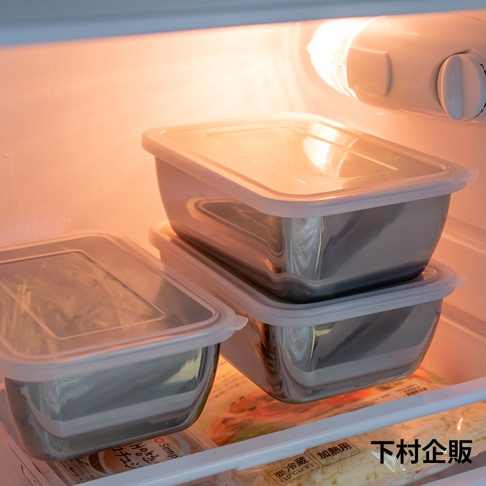 冰箱內部明亮的暖光下，擺放著數個不鏽鋼材質的長方形保存盒。其中一個容器獨立放置於左側，另外兩個則垂直堆疊於右側。這些保存盒均配有半透明的白色塑膠密封蓋，表面反射出冷色調金屬光澤。盒底下方可見部分食材包裝，右下角處印有黑色繁體中文字樣下村企販。