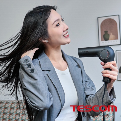 一位女性手持黑色TESCOM摺疊吹風機，正將吹風機對著自己的頭髮。