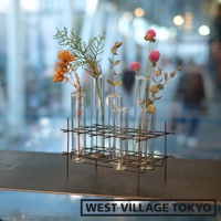 金屬網架上的多個玻璃試管花器，內插有乾燥的橘色花朵、綠色植物和粉紅色球狀花朵。