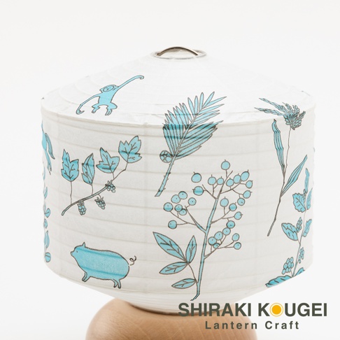 白色紙質提燈，繪有藍色線條的植物圖案，包括葉子、漿果和蕨類植物，以及一隻小豬和一隻猴子。提燈頂部有金屬提環，底部為木質支架。