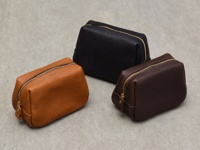 職人手作皮革Organ拉鍊收納包，共三色：淺棕色、深棕色、黑色。包身為荔枝紋皮革材質，配有金色拉鍊和同色系皮革拉環，底部與側邊有縫線細節。