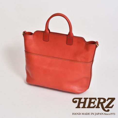 橘紅色皮革製成的大容量兩用托特包，有手提和側肩背的設計，包身簡潔，有明顯的縫線裝飾，展現職人手作質感。