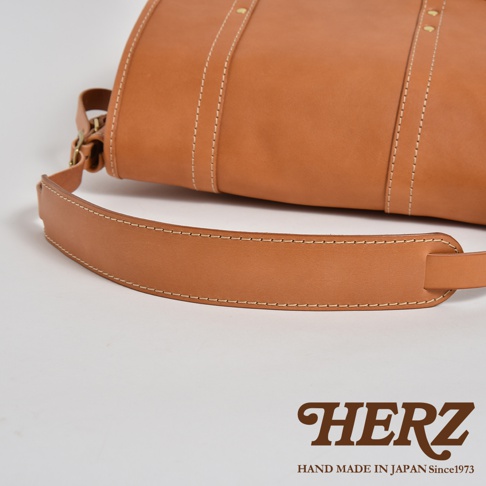 職人手作皮革復古郵差包，採用天然棕色皮革，以白色縫線點綴，展現精緻工藝。包包設計簡約，帶有可調節的寬版皮革背帶，適合日常攜帶。