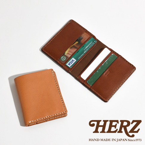 品牌HERZ的皮革證件夾，內含Visa卡，旁邊還有一個較小的淺棕色皮革錢包，背景是白色的。