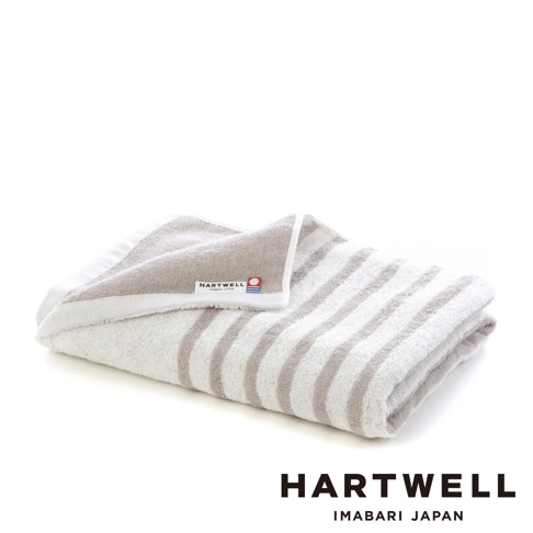 一條白色與灰色條紋的今治毛巾，材質柔軟，標籤印有「HARTWELL IMABARI JAPAN」字樣。