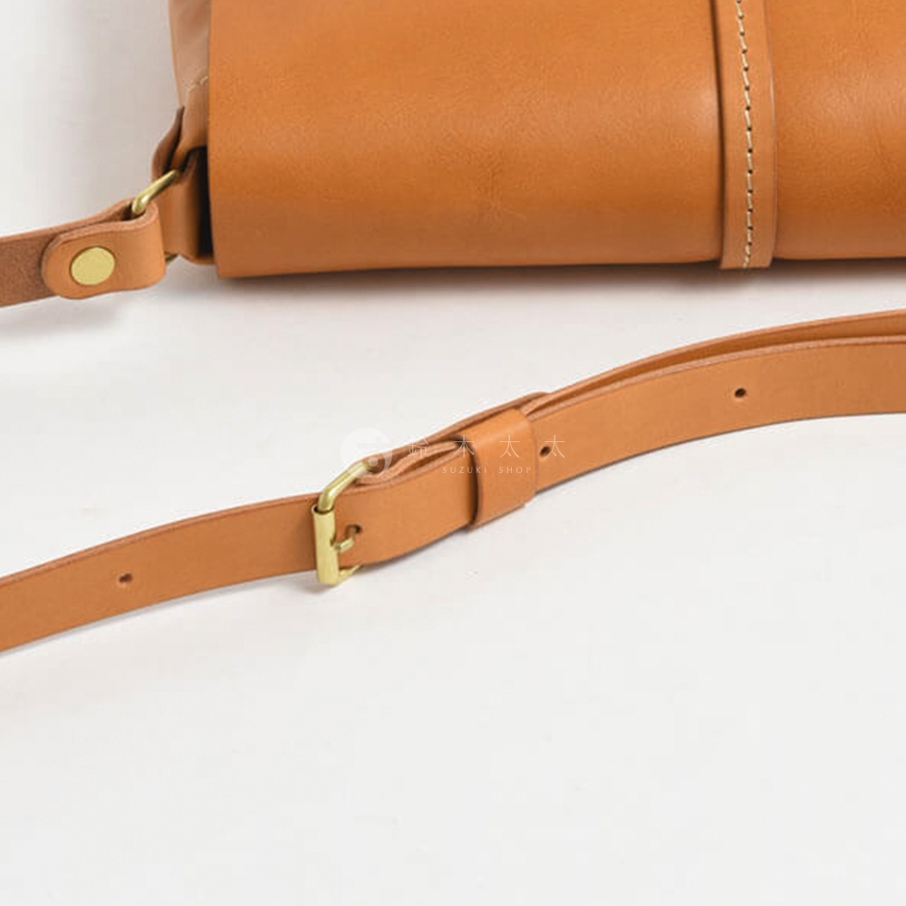 模式B： 近拍皮革馬鞍包的肩帶，有金色扣環和調節帶，肩帶上有 SUZUKI SHOP 的浮水印。