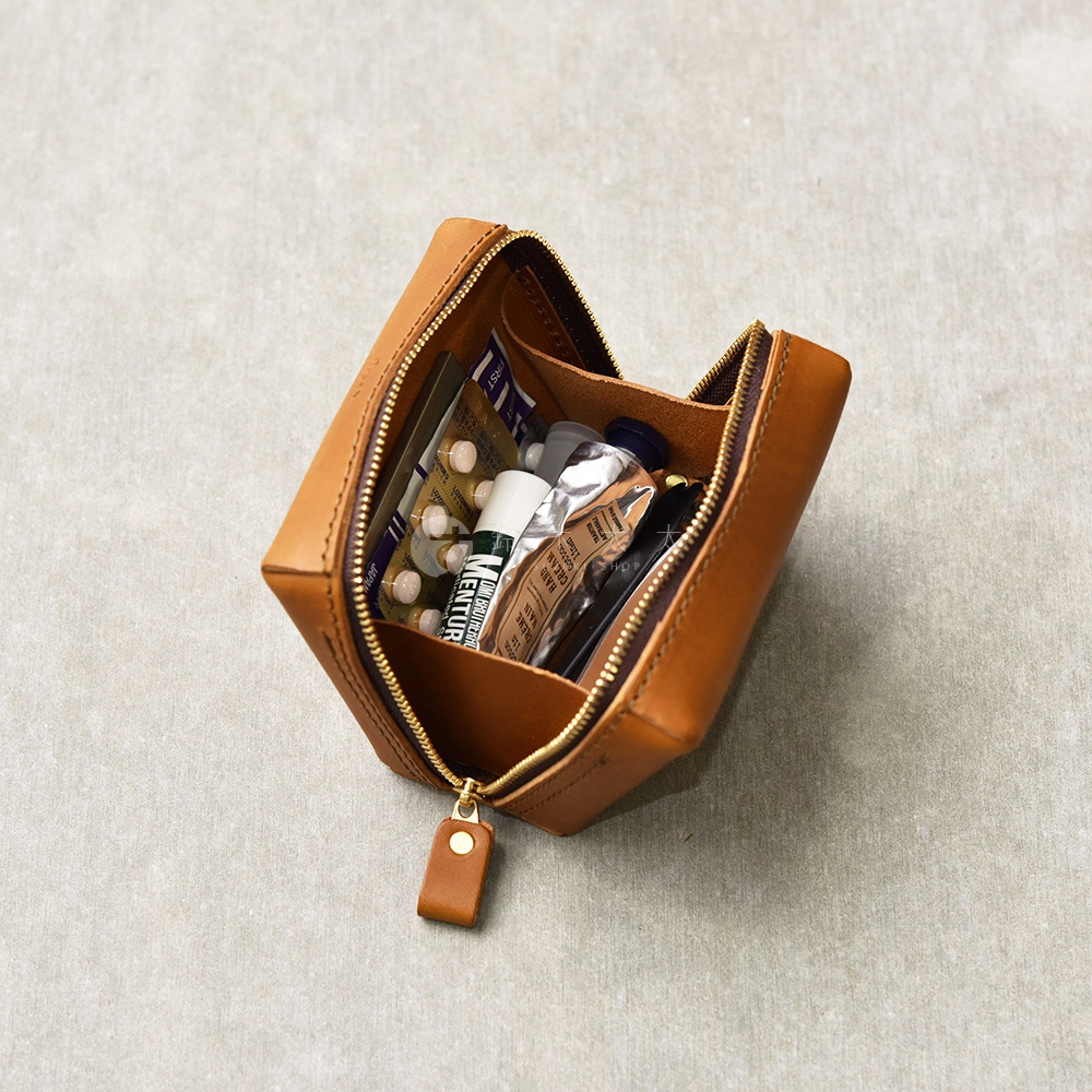 一個打開的棕色皮革箱型收納包，裡面裝有藥丸、藥膏和筆。