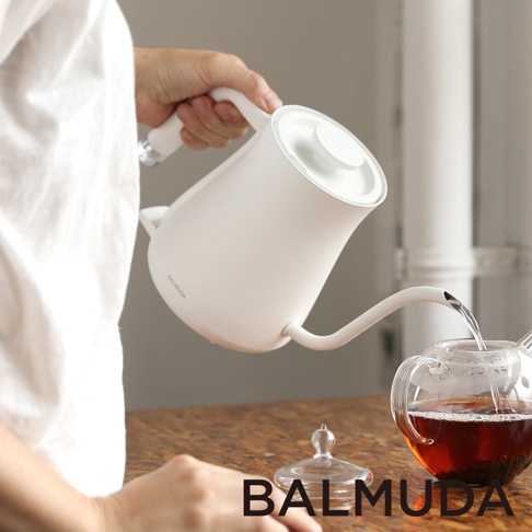 手持白色簡約手沖壺，壺嘴細長，正在往透明玻璃茶壺中注入熱水。
