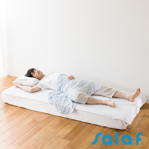 一名男子仰臥在白色單人睡墊上，蓋著藍白色條紋毛毯，頭枕在白色枕頭上。睡墊為白色，邊緣有淺藍色滾邊。