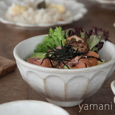 淺米色陶瓷丼碗，碗身帶有六個凹槽紋飾，盛有鮭魚、酪梨、海苔絲、芝麻及生菜等日式料理。