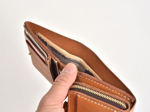 職人手作皮革直式卡片收納雙折短夾，原色皮革材質，內含日圓紙鈔及信用卡，以精緻縫線製作，展現皮革質感。