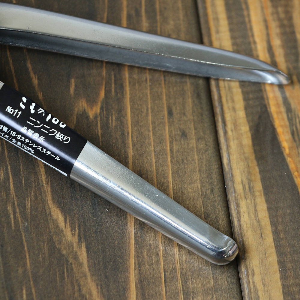 銀色不鏽鋼壓蒜器，部分有黑色標籤，標示「No.11」、「品質表示」、「材質/18-8不鏽鋼」、「尺寸/全長150%」。