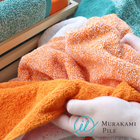 Murakami Pile 的字樣與藍色圓形標誌，疊放著觸感柔軟的橘色毛巾。