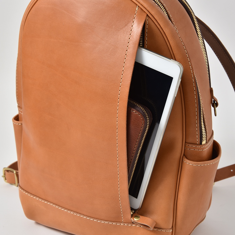 職人手作皮革多功能後背包 R-21，棕褐色，展示側邊拉鍊口袋內側放置了一台白色平板電腦及一個棕色皮夾。