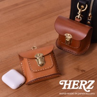 兩個職人手作皮革耳機收納包，其中一個為淺棕色，另一個為深棕色，皆有金屬釦和縫線細節。