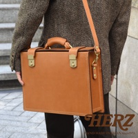 職人手作皮革兩用機師箱，以堅固的焦糖棕色皮革製成，配有金色鎖扣和雙提把，可肩背或手提。