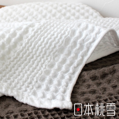 今治鬆餅毛巾，織有獨特蜂窩狀紋理，觸感柔軟。此為白色毛巾，疊放在深棕色毛巾之上，展現其立體織法。