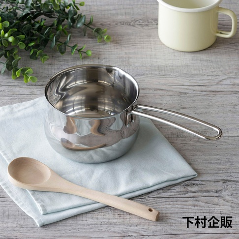 一個12公分的不鏽鋼牛奶鍋，鍋身閃亮，帶有一個長柄，鍋內有刻度。旁邊放著一塊淺藍色布和一個木勺。