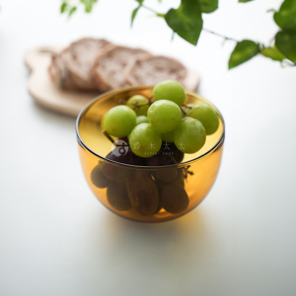 琥珀色玻璃點心碗裝著綠色和紫色葡萄，碗的背景是切片麵包和木砧板。