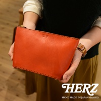 一橙色皮革手拿包，有拉鍊封口及品牌壓紋，由雙手持握。