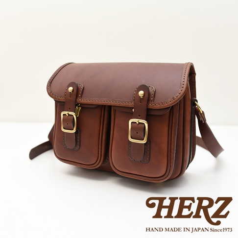 日本HERZ手工皮革經典雙扣郵差包，棕色皮革搭配金色釦環，雙口袋設計，整體呈現復古質感。