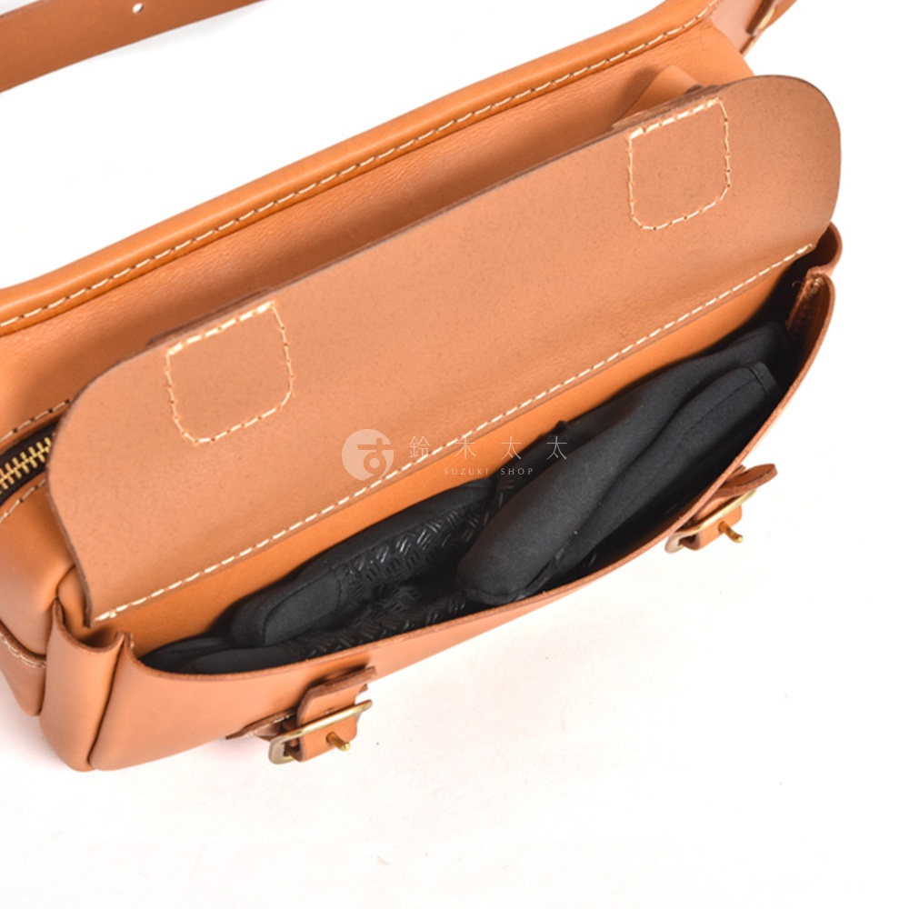 職人手作皮革騎士隨身斜背包，展示棕褐色皮革材質，包身設有拉鍊與金屬扣環，內部空間可見黑色物品。