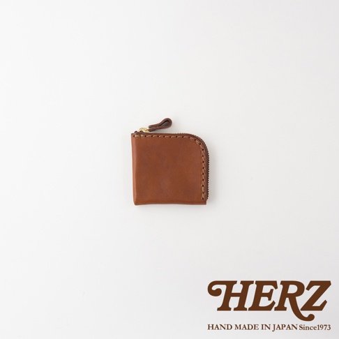 日本HERZ職人手作皮革零錢包，選用質感咖啡色皮革製成，採用L型拉鍊設計並配有皮革拉環，外觀簡約精緻，右下角印有HERZ HAND MADE IN JAPAN Since1973品牌標誌。