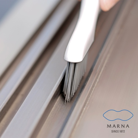 白色塑料手柄的縫隙清潔刷，帶有密集、灰色的細長刷毛，正在清潔銀色金屬表面上的縫隙。