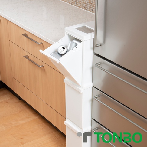 白色三層抽屜式分類垃圾桶，頂層抽屜打開，內有數個鋁罐。垃圾桶緊鄰廚房木紋櫥櫃和不銹鋼冰箱。