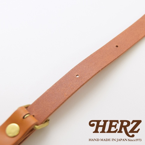 HERZ 品牌標誌，下方為 HAND MADE IN JAPAN Since1973 字樣，圖片為棕色皮革肩帶細節，帶有金屬扣環和調整孔。
