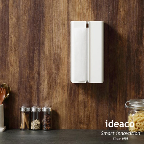 白色ABS材質的壁掛/桌上兩用擦手紙架，設計簡潔，可容納一疊擦手紙，掛置於木紋背景牆上。