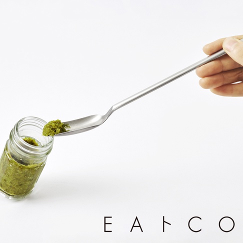 一只手拿著一支細長的銀色金屬長柄勺，勺頭舀著綠色的醬料，旁邊是一個裝有綠色醬料的透明玻璃小罐。
