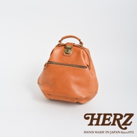 職人手作皮革輕旅行後背包，採用溫潤的淺棕色皮革，帶有復古風格的銅色金屬鎖扣和拉鍊，包身線條圓潤，質感厚實，適合日常或短途旅行攜帶。