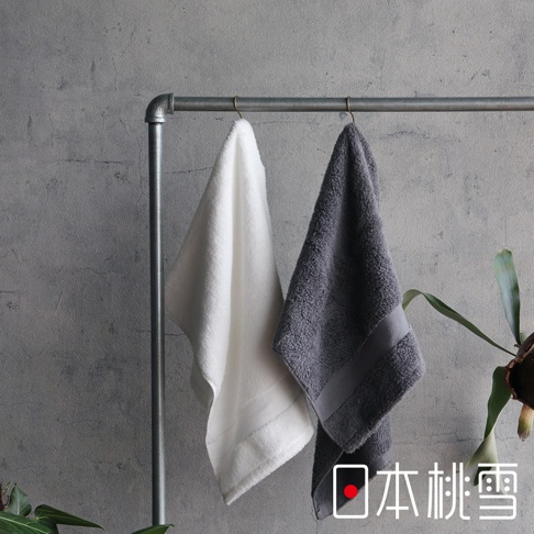 兩條今治匹馬棉浴巾，一條為白色，另一條為灰色，皆懸掛於金屬毛巾架上，背景為水泥牆面。