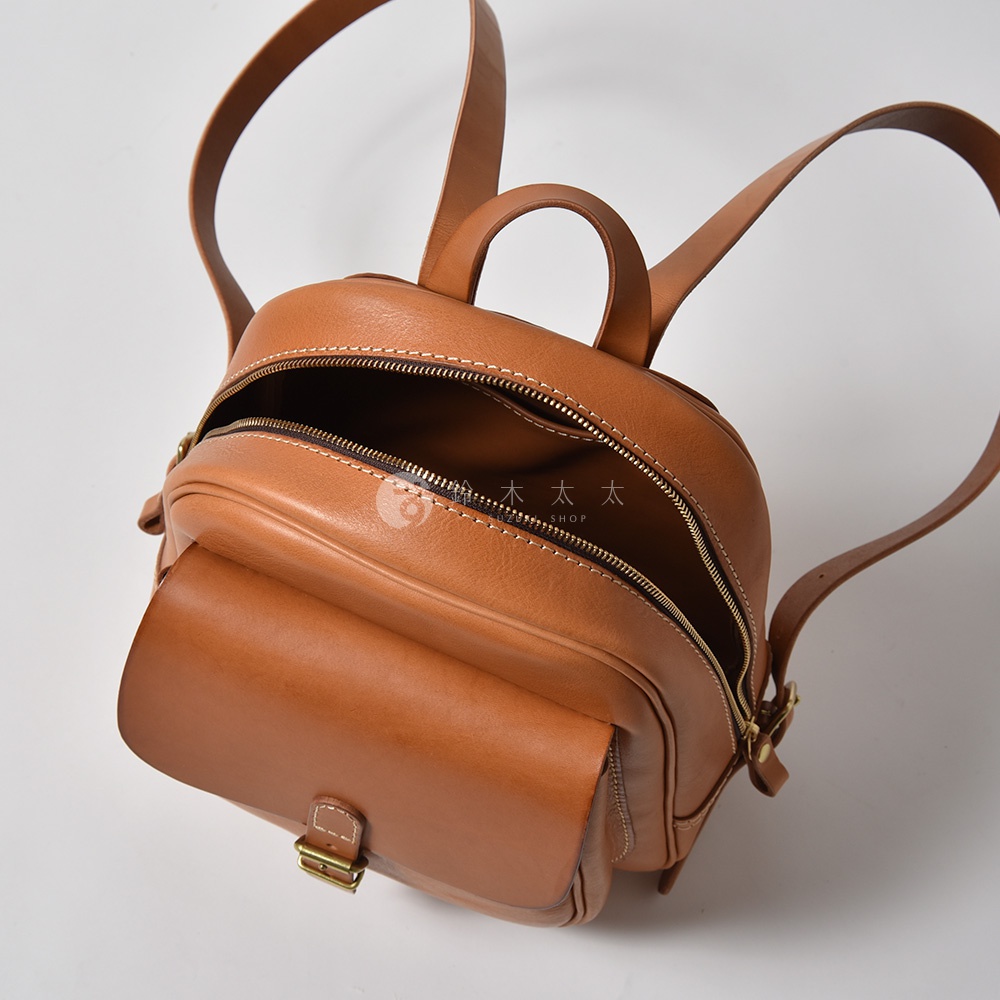棕色皮革迷你後背包，立體前袋配有金屬釦帶，頂部拉鍊開口，可見白色縫線細節，附有兩條肩帶。