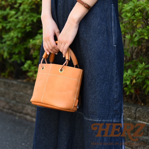簡約焦糖色皮革手提午餐袋，大開口設計，配有皮革加厚提把及金屬孔眼。袋身有職人縫線裝飾。