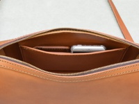 職人手作皮革單肩包內部，展示了拉鍊開合、一個手機隔層，以及光滑的棕色皮革材質，縫線清晰。